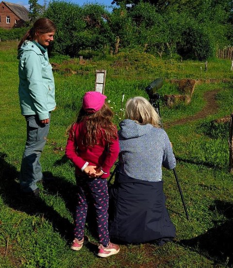 Zwei Frauen und ein Kind sind mitten in einem Naturgarten. Vor der einen Frau steht ein Spektiv zum Vögel beobachten.